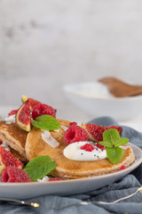 Pancakes with raspberries, figs, yogurt, coconut zest, honey and mint leaves on a plate.
