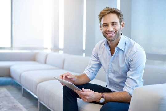 Young businessman smiling while on couch with digital tablet