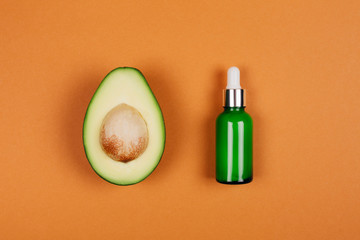 Half avocado with bone and green bottle with beauty oil on orange background. Flat lay style.