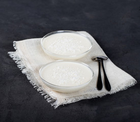 Vanilla Panna cotta in a glass dish, Italian dessert creamy jelly with coconut shavings on a dark background