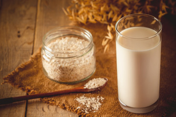Glass of oat milk on a wooden background. Lactose-free vegetable diet milk. Gluten free oat drink...