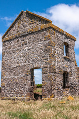 Fototapeta na wymiar Stanley, Tasmania, Australia - December 15, 2009: Hightfield Historic Site. Corner of gray stone building ruins against blue sky with white clouds, green yellow grass in front.