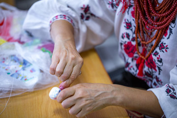 Hands of a craftsman in the Ukrainian folk costume (embroidery and coral necklace) conducting a rag doll master class.