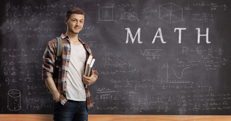 Male student with a backpack and books with a blackboard written with math formulas