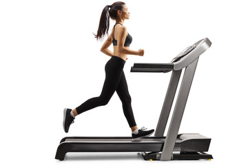 Full length profile shot of a young slender woman running on a treadmill isolated on white...