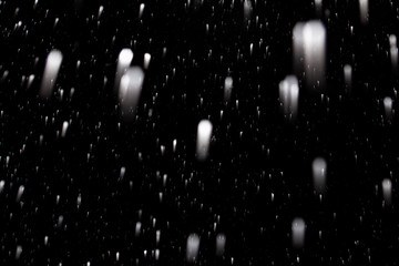 flakes of snow falling fast against a black sky, the front and background blurred with a bokeh effect