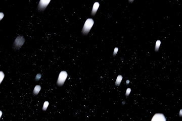 flakes of snow falling fast against a black sky, the front and background blurred with a bokeh effect
