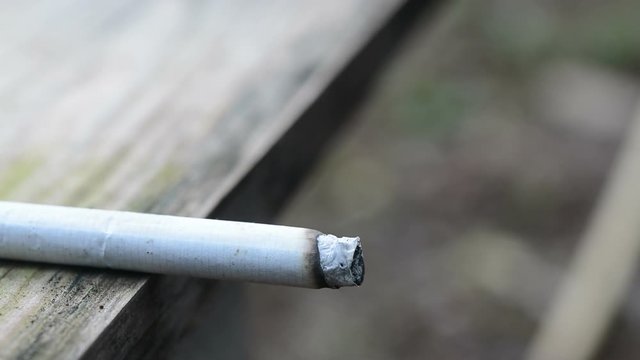 Close up cigarette burning with smoke on wood plank