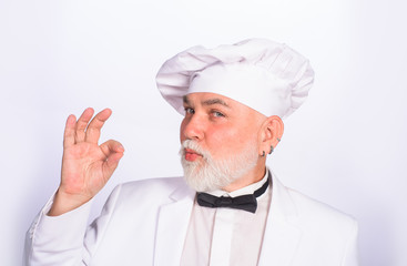 Male chef in white uniform with perfect sign. Cook with taste approval gesture. Professional chef man showing sign for delicious. Serious satisfied bearded chef, cook or baker gesturing excellent.