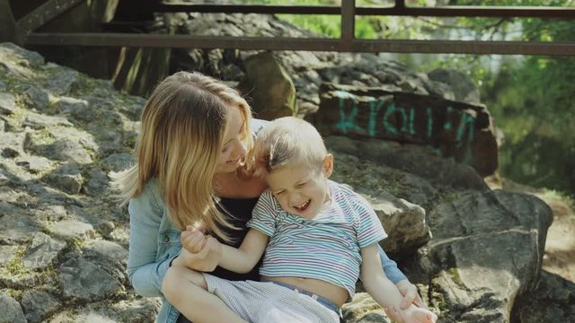 Beautiful young mom and cheerful adorable blond boy are playing, having fun. Woman loves her son. Beautiful young mom and cheerful adorable blond boy are playing in the park