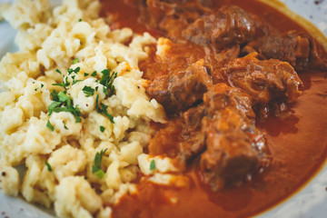 Traditional hungarian and austrian dish - beef goulash with garnish egg noodles, mashed potatoes in...