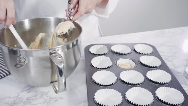 Step by step. Scooping batter with batter scooper into cupcake pan lined with paper cupcake liners.