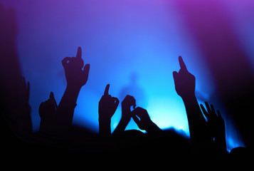 Audience with hands raised at a music festival and lights streaming down from above the stage. Crowd raising their hands, dancing and enjoying great the concert.