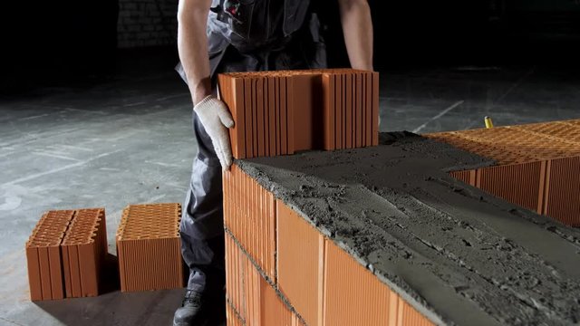 Industrial bricklayer worker placing bricks on cement while building walls. Stock footage. Close up of a man in protective gloves putting heavy brick block to form a layer.