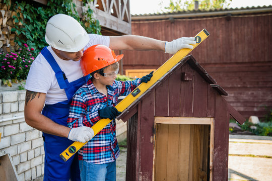 Turning their visions into reality. Cheerful young male carpenter embracing his son while measuring dog house with building level