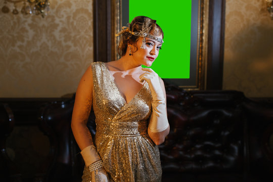 a woman in a gold dress in the image of 20s, looking at the camera against the background weighs a picture of a lame man, long gloves are on the head of the diodema