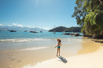 Child playing in the sand at Abraaozinho Beach with taxi boat and blue waters in Abraao, on the tropical Ilha Grande, Angra dos Reis, in the south of Rio de Janeiro Brazil
