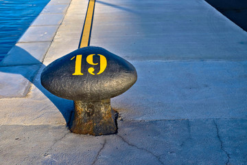 Number 19, nineteen, stencil yellow digit painted on a big commercial harbor bollard.
