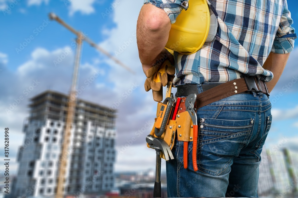 Wall mural Male worker with a tool belt on construction background