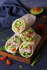 Turkey wraps with avocado, tomatoes and iceberg lettuce on chopping board. Tortilla, burritos,...