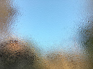 Rain drops on a glass window with blurred blue sky background, view through a wet window .