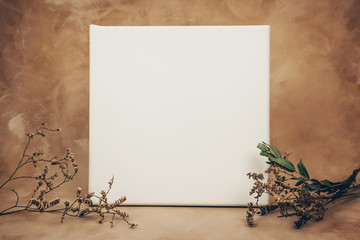 Blank canvas and bouquet of dried flowers on beige background. Poster frame mockup.