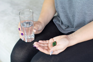 Young girl holding a glass of water and vegan pills, detail