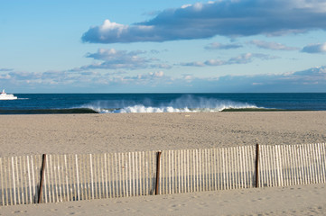 Heavy surf crashing into a sandy shoreline at Belmar Beach, New Jersey, USA, under a partly cloudy sky