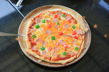 Delicious Hawaiian Pizza served on wood tray against on black table.