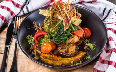 A dish of vegetables, Halloumi, Pumpkin, Cherry Tomatoes, Pepper and Eggplant, Pumpkin stacked up on a dark blue plate.