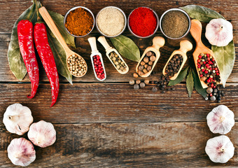Red hot chili pepper, different pepper in ceramic cups, peppercorn in scoops, bay leaves and garlic on wooden background. Text space. Top view.