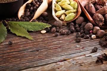 A variety of cardamon and pepper in wooden scoops with dry bay leaves on wooden background. Copy space.