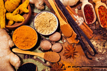 Spices on wooden background. Different peppercorns, ginger, turmeric, saffron,  bay leaf, cloves, kalonji, nutmeg, anise, cinnamon and vanilla pods. Top view.