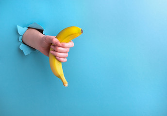 Banana in a woman's hand from a hole in paper on a blue background