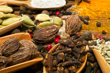 Cardamon and cloves in wooden scoops, spices on wooden background. 