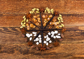 Celtic wheel of a year made of sweet spices. Green and brown cardamom, star anise, vanilla pods, crystals of sugar and salt on wooden background. Top view. 