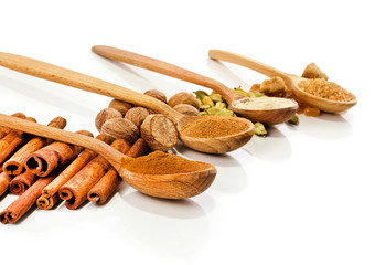 Nutmeg, cinnamon, cardamom, brown sugar and powder of nutmeg, cinnamon, cardamon, brown sugar in a wooden spoons isolated on white background.