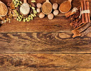 Brown sugar crystals, cardamom, nutmeg, cinnamon sticks, star anise and powder of nutmeg, brown sugar in a wooden spoon on wooden background. Sweet spices. Text space.