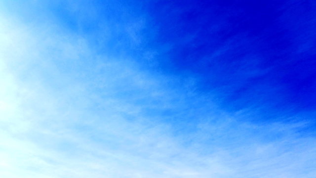 The blue sky cloudscape shot with interweaving clouds. Clean blue area with just a wisp cloud for usage like a backdrop in your designing  area. Royalty free stock photo.