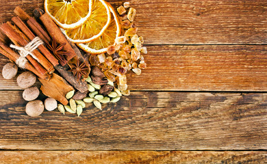 Slices of dried orange, brown sugar crystals, cardamom, nutmeg, cinnamon sticks and star anise on wooden background. Sweet spices. Top view. Copy space.