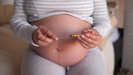 Close-up of a pregnant woman holding an insulin syringe and an ampoule of insulin. Diabetes and pregnancy health, sugar control.