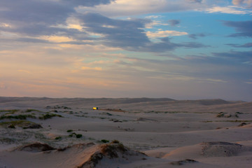 Wide boundless flat desert and a point of a white car driving along it far away. Twilight. Stockton Sand Dunes near the coast, Worimi Regional Park, Anna Bay, Australia