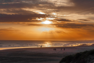 The bright rays of the sun make their way through the clouds. High contrast brown-orange sunset on the wide ocean beach, twilight. Stockton Sand Dunes, Worimi Regional Park, Anna Bay, Australia