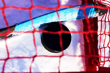 Hockey stick with a blue ribbon and a black puck in the goal after a goal. Top view through the grid. Winter street sports