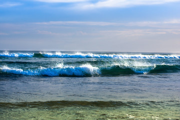 Two low ocean waves, rushing on the shore. Foam on the ridges glows in the sun. Water changes color from dark blue to green at the shore. Anna Bay, Australia
