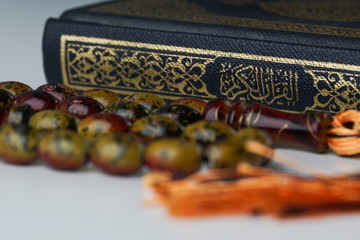 Close up on side of Holy Al Quran with written arabic calligraphy and wooden beads or tasbih on white background.