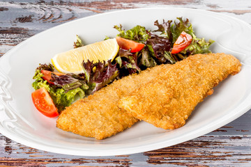 Breaded trout fillet with vegetables on a white plate