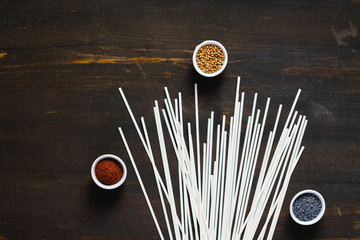 Fototapeta na wymiar Different kind of spices and raw udon noodles on dark wooden background. Collection of spices coriander poppy sumac and sesame. Asian or Indian food concept.