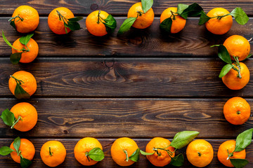 Tangerines with leaves frame on dark wooden background top-down copy space