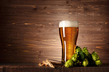 Beautiful tasty beer with foam in glass glass with hops cones and wheat ears on dark wooden table...